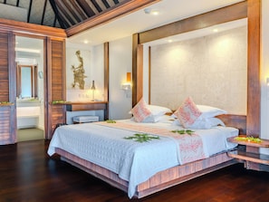 A spacious bedroom with a large bed, a wooden headboard, a nightstand, and a wall-mounted lamp. - Manava Beach Resort & Spa Moorea (Moorea-Maiao)