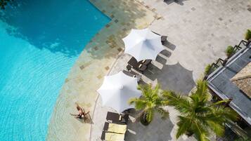 Vista aérea de una zona junto a la piscina con sillones, sombrillas y palmeras.