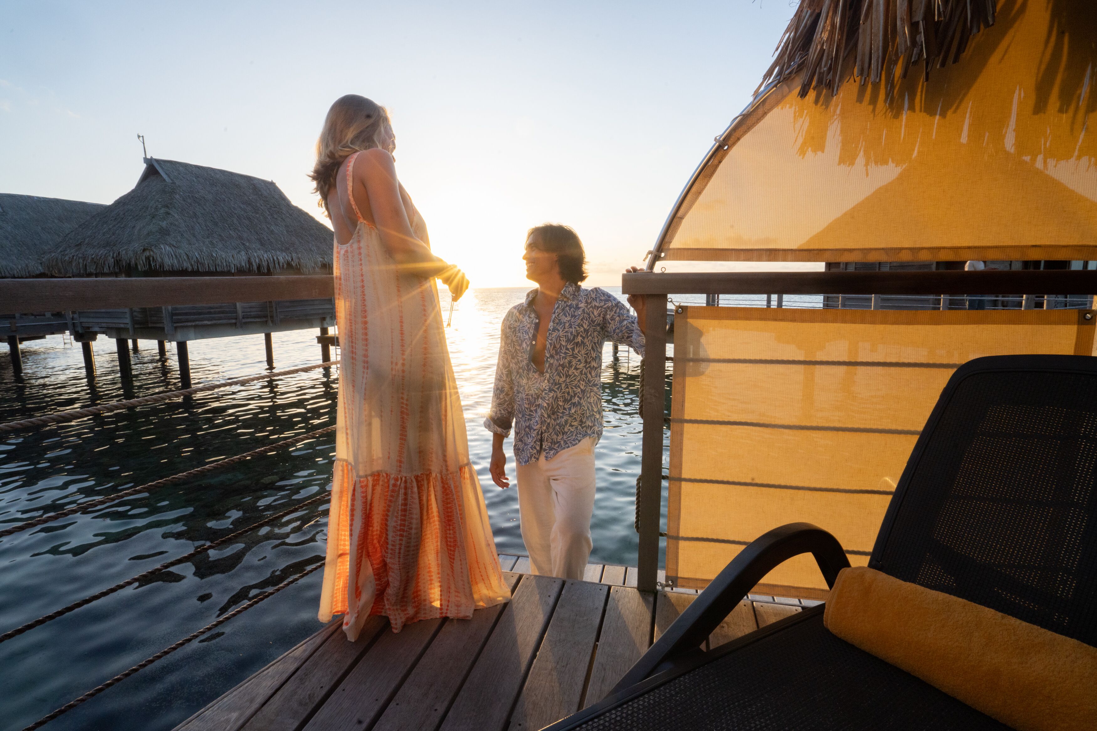 A couple on a wooden deck overlooking a body of water with overwater bungalows in the background.