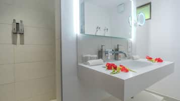Un baño moderno con un espejo grande, zona de ducha y tocador con lavamanos.