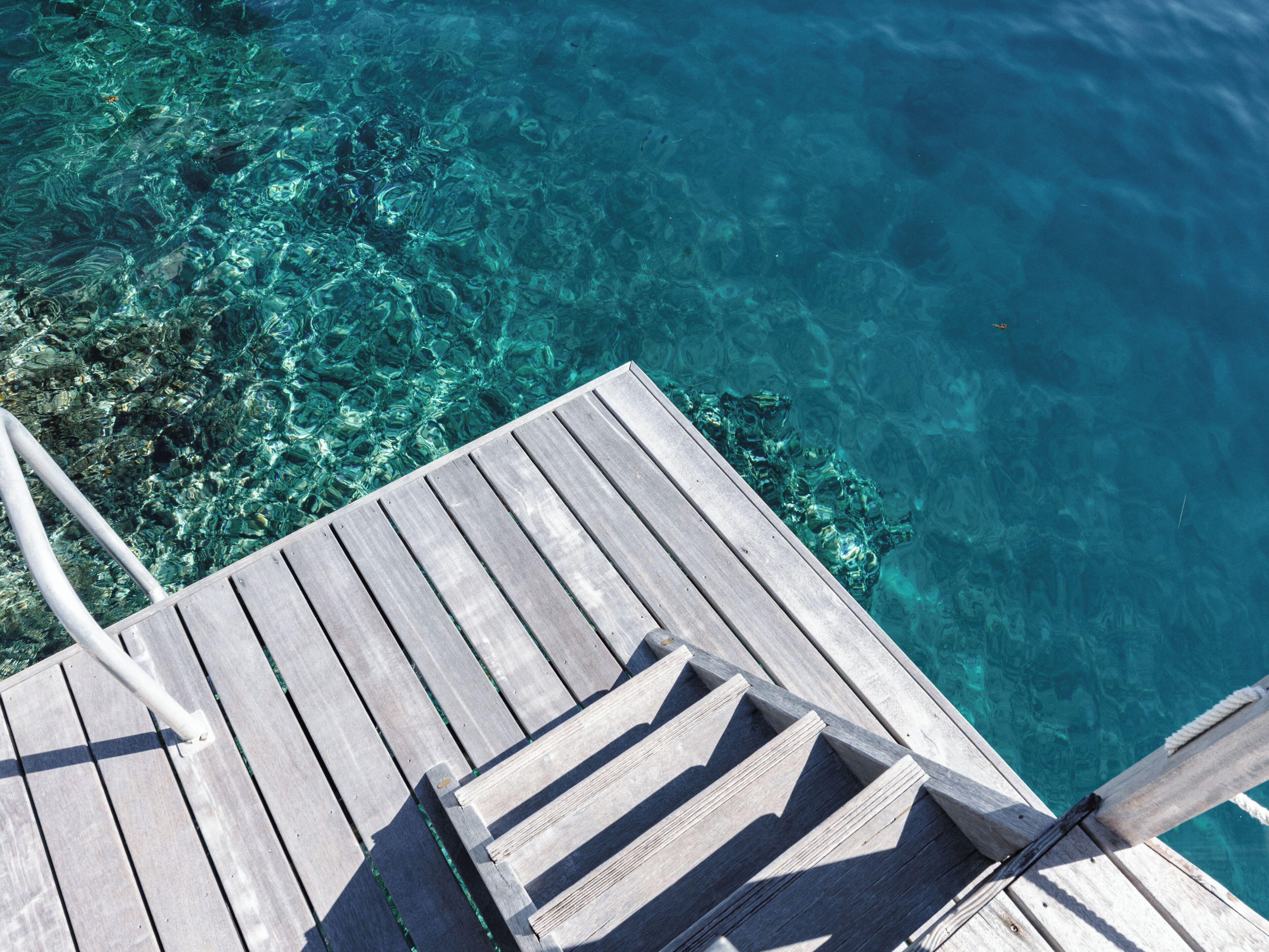 A wooden deck leading into clear blue water with visible underwater rocks.