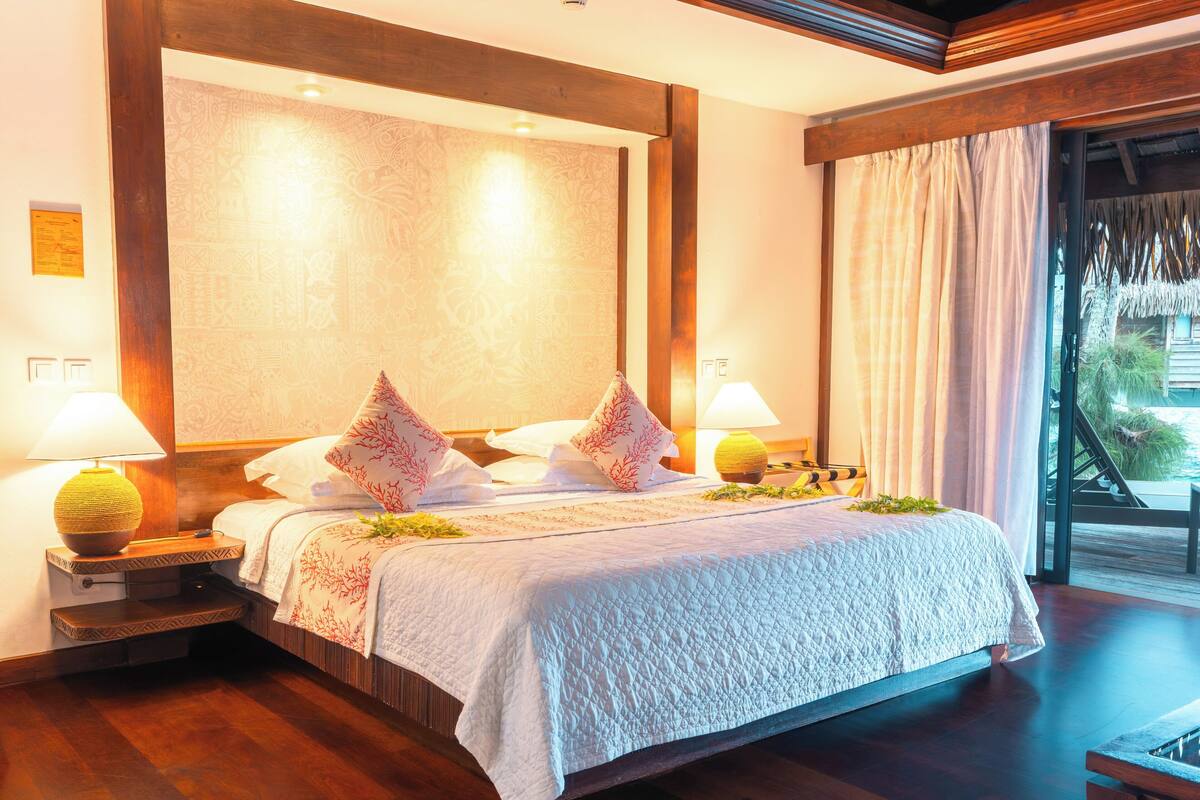 A hotel room with a large bed, two bedside lamps, a wooden headboard, and a view of the outdoors.