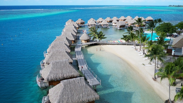 Des bungalows sur pilotis avec toits de chaume, une eau turquoise cristalline et une plage de sable.