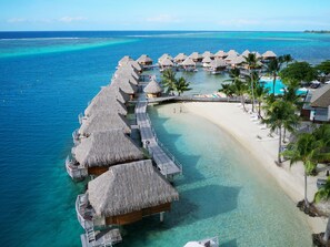 An overwater bungalows with thatched roofs, clear turquoise water, and a sandy beach. - Manava Beach Resort & Spa Moorea (Moorea-Maiao)