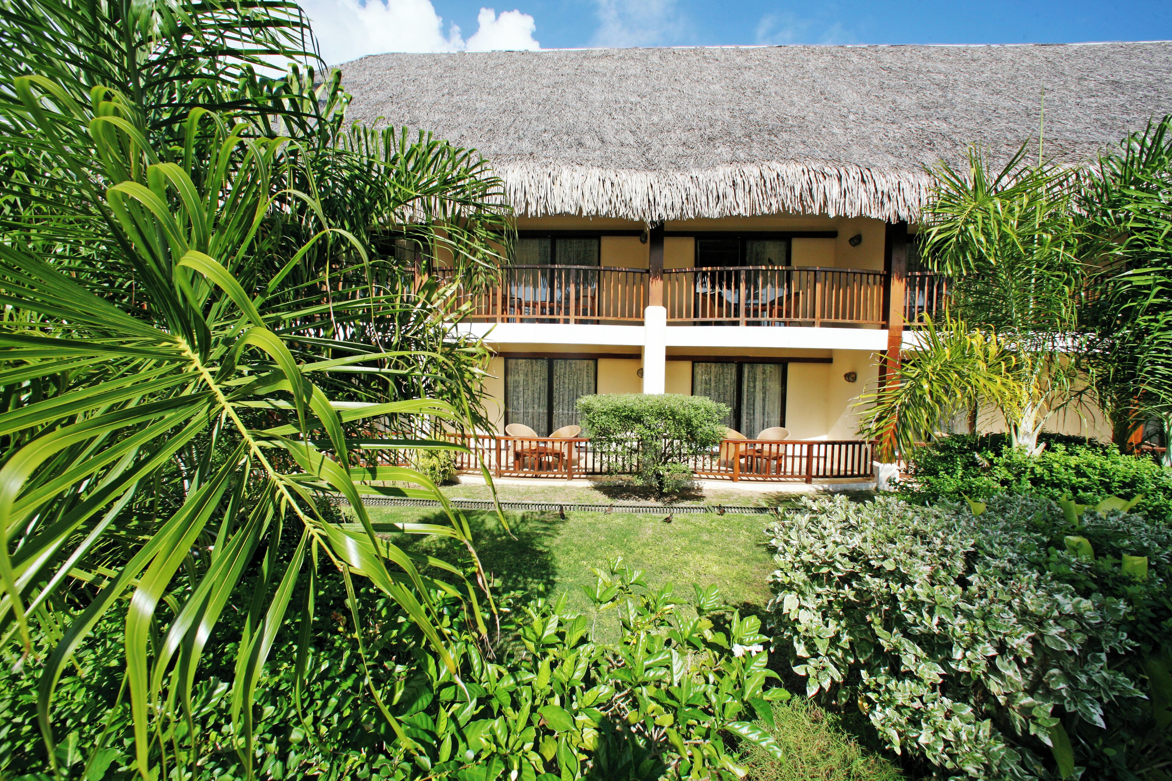 A hotel with a thatched roof, a balcony with seating, and lush greenery.