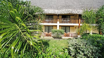 Een hotel met rieten dak, een balkon met zitplaatsen en weelderige begroeiing.