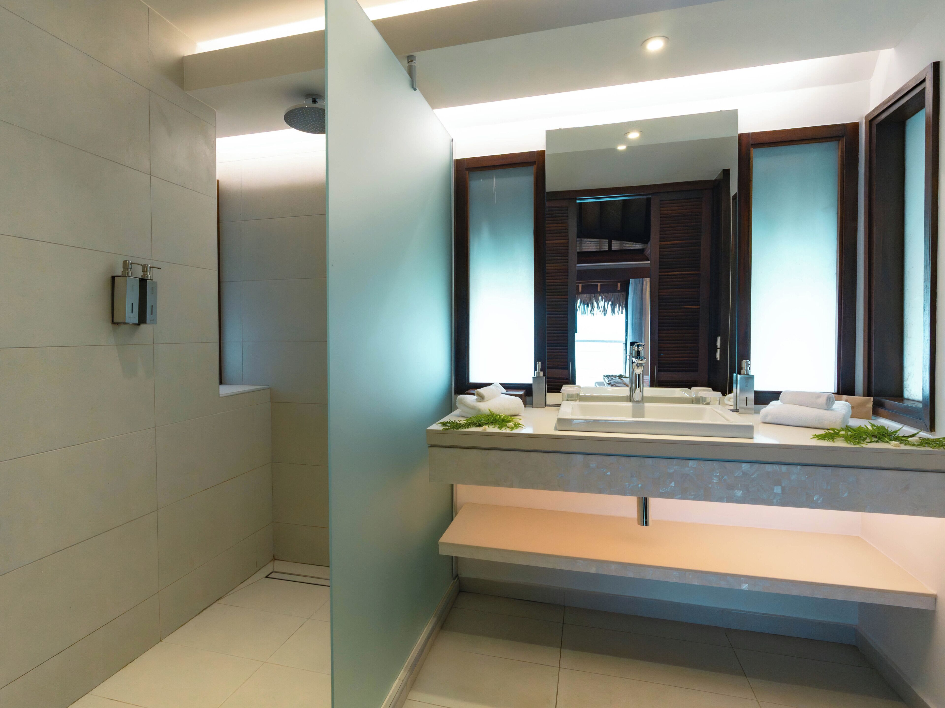 A modern bathroom with a large mirror, two sinks, and a shower.