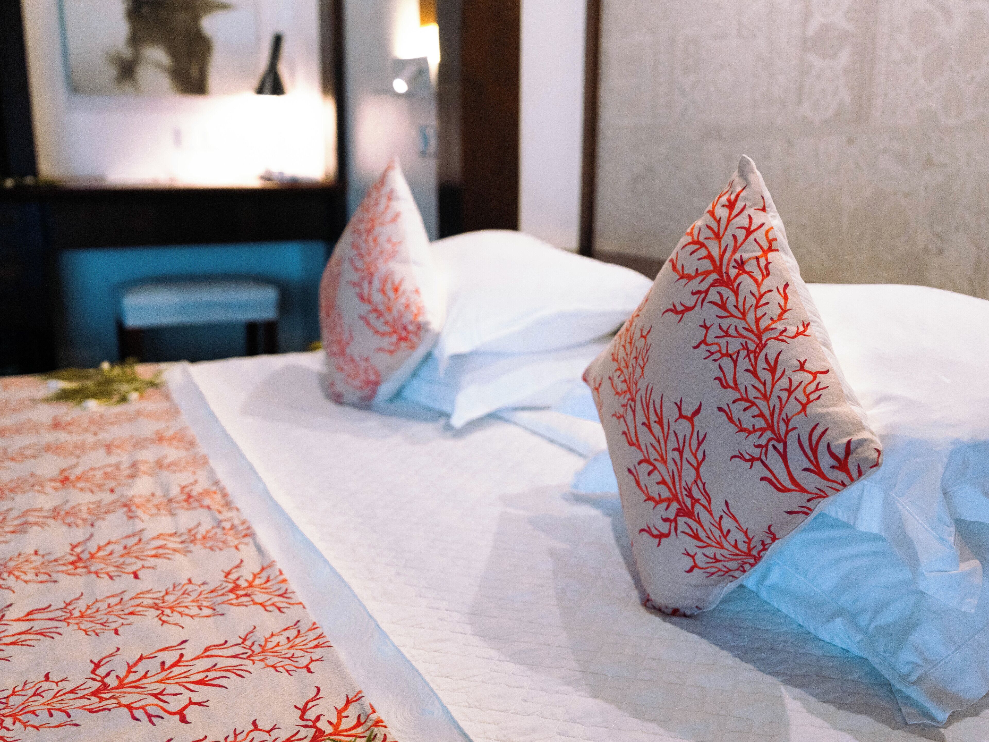 A neatly made bed with white linens and red coral-patterned pillows.
