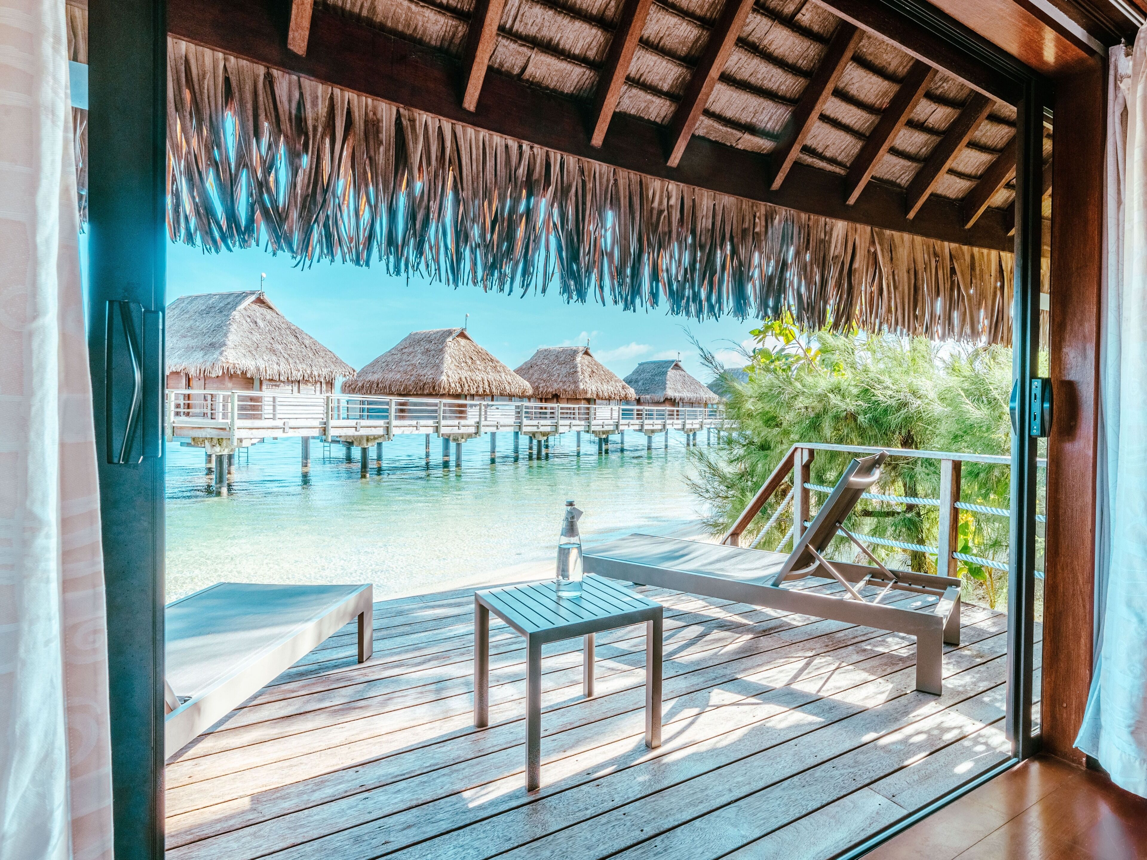 An overwater bungalows with thatched roofs, wooden deck, and a clear view of the ocean.