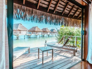 Bungalows sobre el agua con techos de paja, terraza de madera y vista despejada del océano.