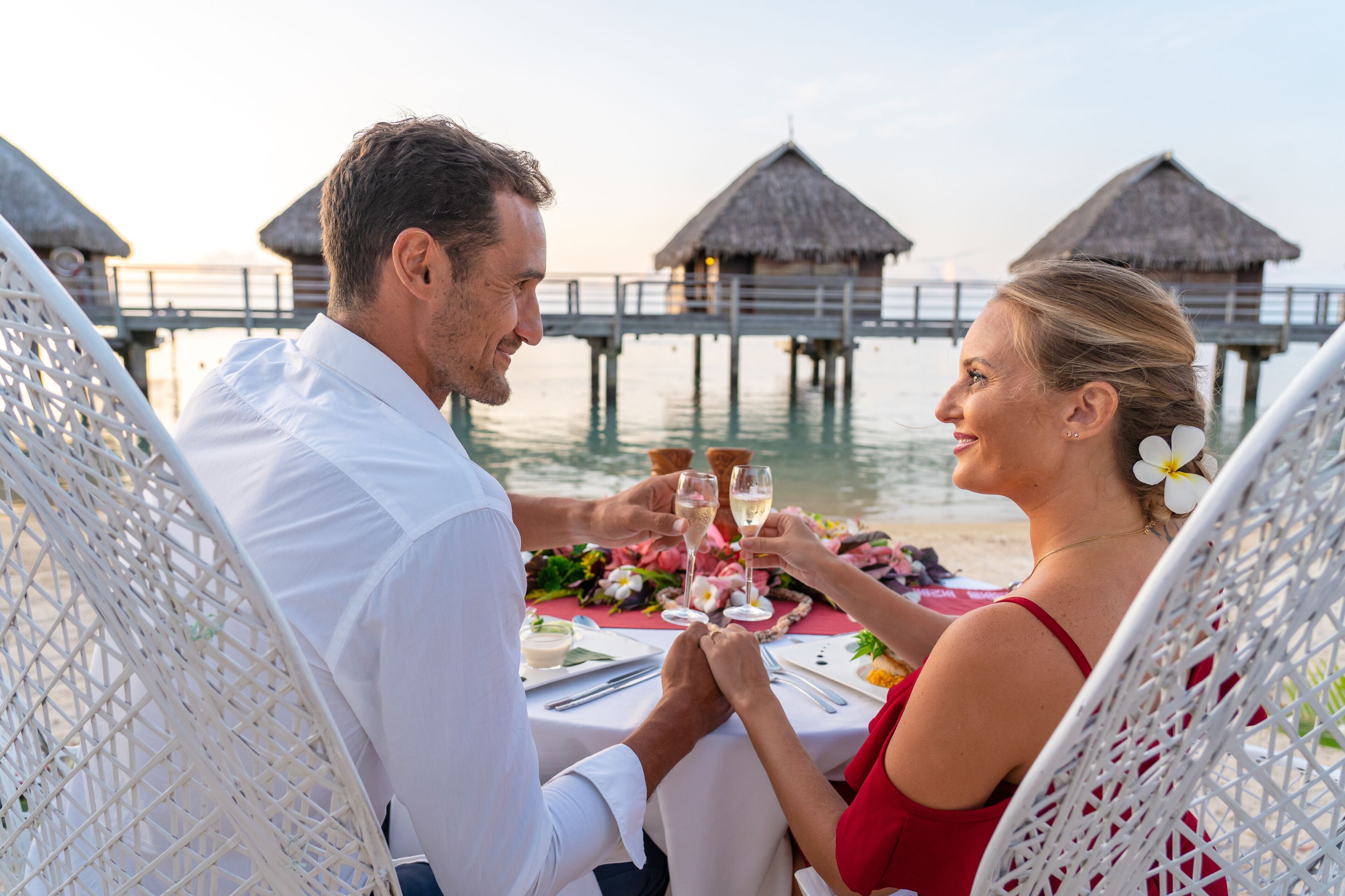 A couple dining at a table with a view of overwater bungalows and water.