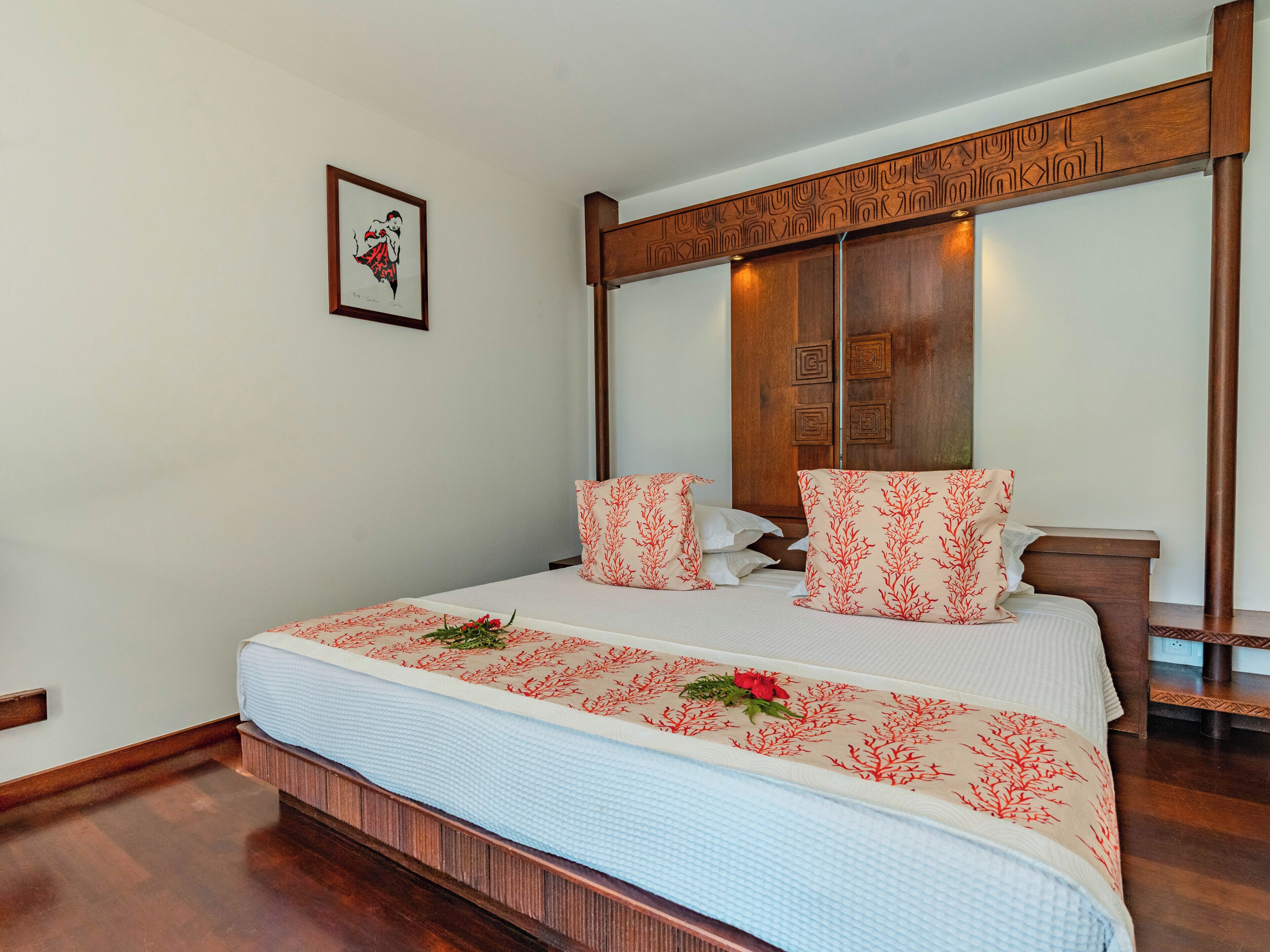 A hotel room with a bed, wooden headboard, and a framed picture on the wall.
