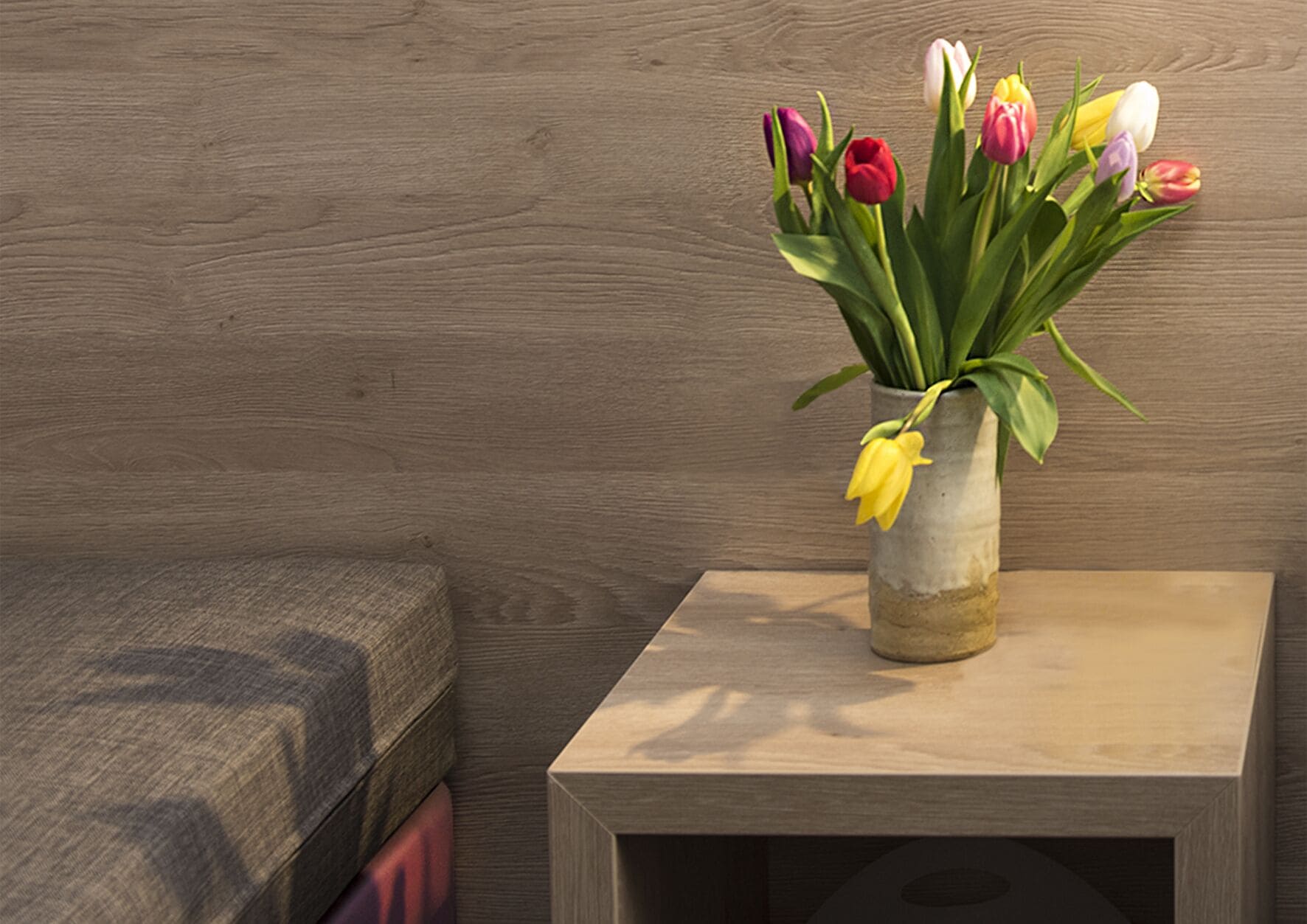 Una pared de madera, una pequeña mesa de madera con un jarrón de tulipanes, y un banco de madera.