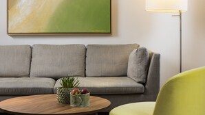 Un salón moderno con un sofá gris, una mesa de centro de madera con objetos decorativos, un sillón amarillo y una lámpara de pie.