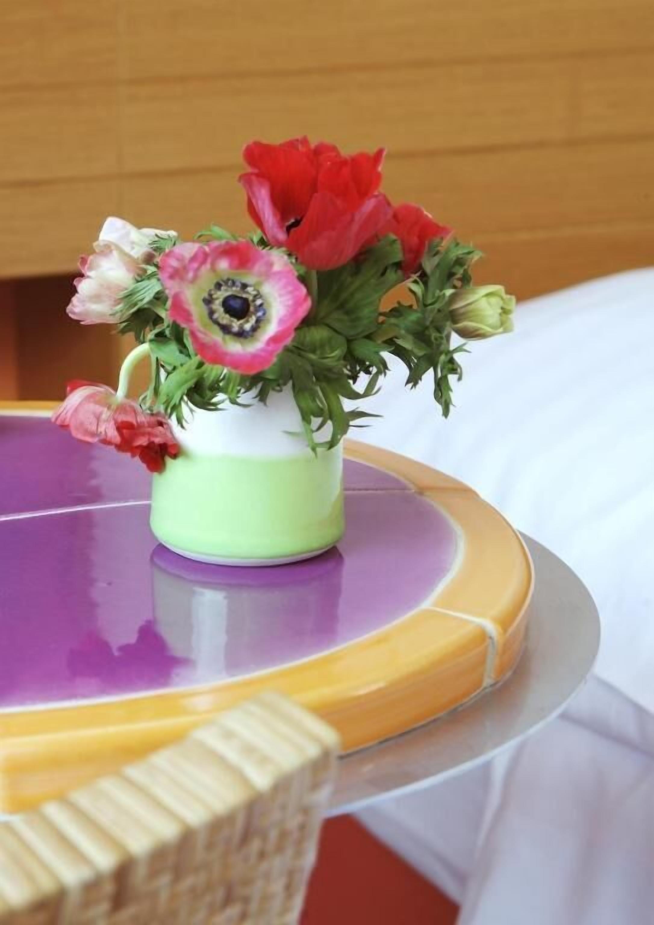 A small green vase with a variety of flowers on a round table.