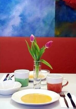 Una mesa con un jarrón de tulipanes, un plato con una sustancia amarilla y dos tazas de té.