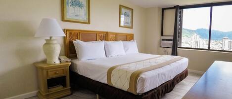 Quarto de hotel com cama, mesa de cabeceira, luminária e janela com vista para a cidade.