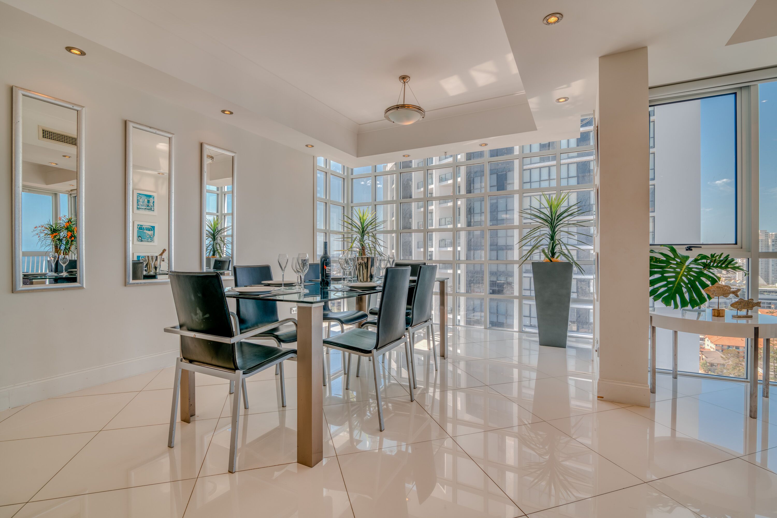 A spacious dining area with a modern glass table, black chairs, and potted plants.