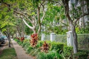 A tree-lined street with a sidewalk, parked cars, and a white fence. - Bel Air on Broadbeach (Broadbeach)