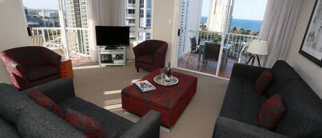 A modern living room with grey sofas, a red patterned ottoman, and a flat-screen TV.