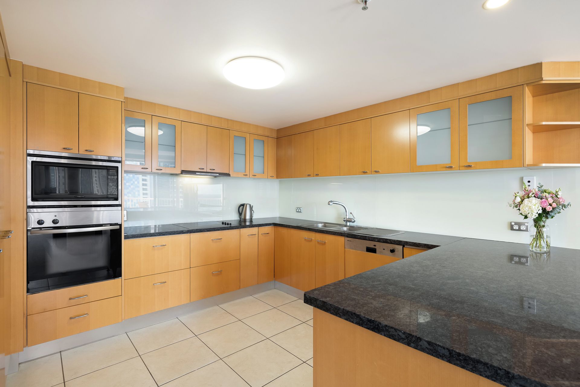 A modern kitchen with wooden cabinets, stainless steel appliances, a black granite countertop, and a vase with flowers.