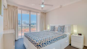 A hotel room with a bed, a nightstand, a ceiling fan, and a view of the city through large windows.