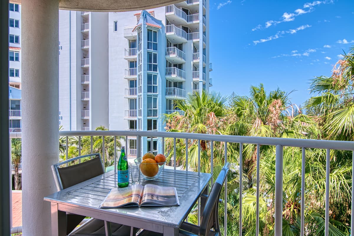 A balcony with a table, a chair, a bowl of fruit, and a bottle of water.