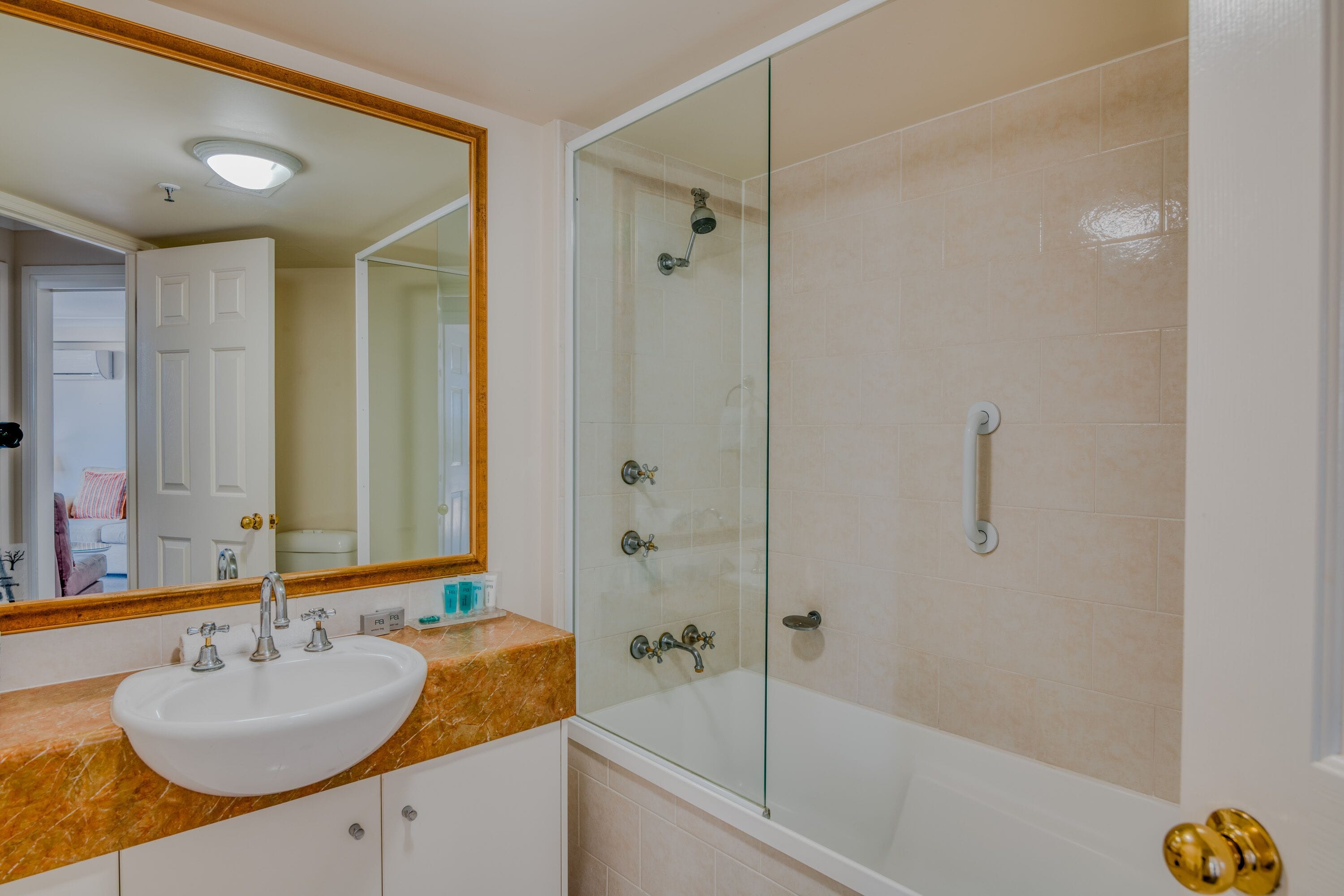 Een badkamer met een witte wastafel, een douche met glazen wanden en een wit bad.