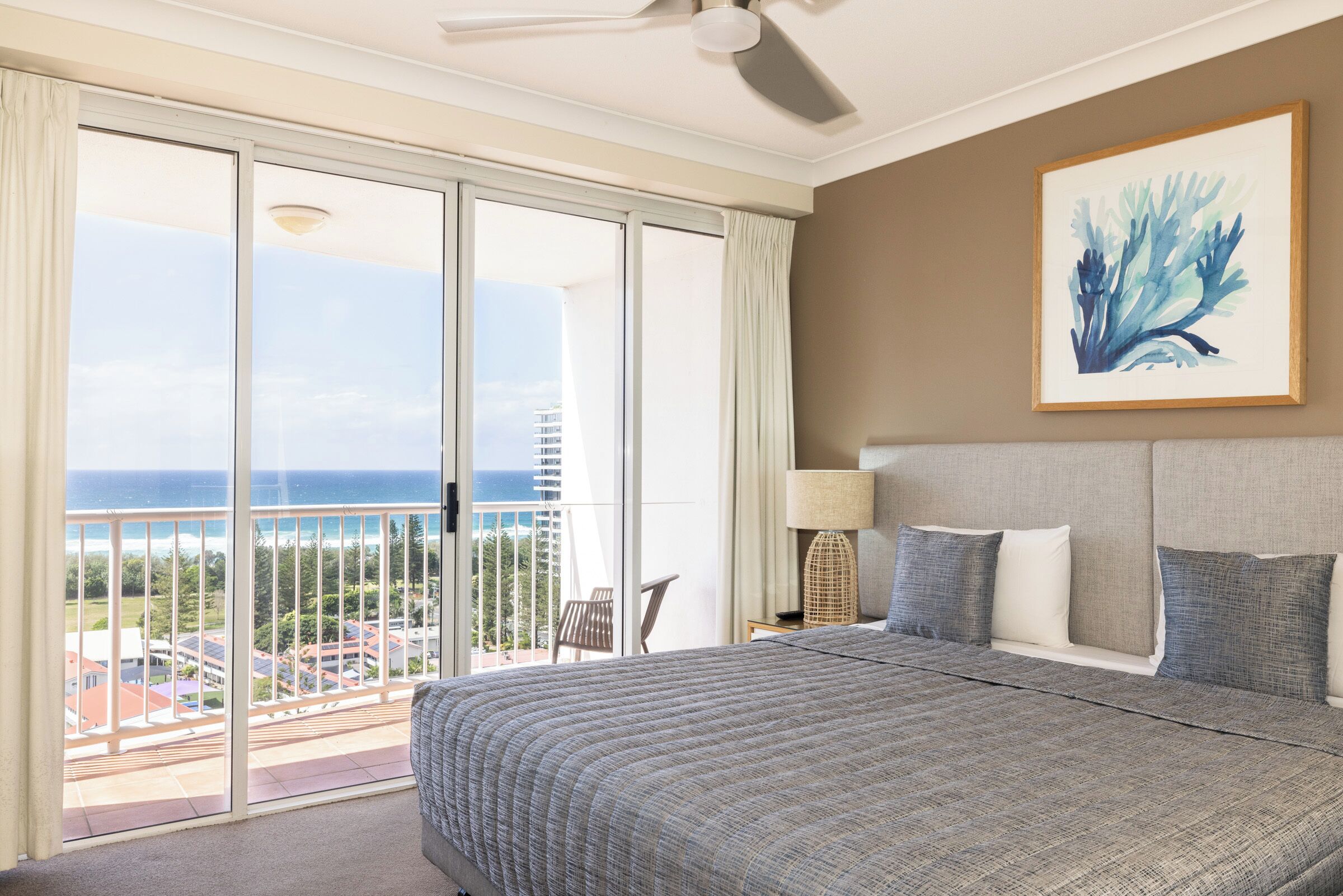 Ein Schlafzimmer mit einem großen Bett, einem Deckenventilator, Meerblick und einem Bild an der Wand.