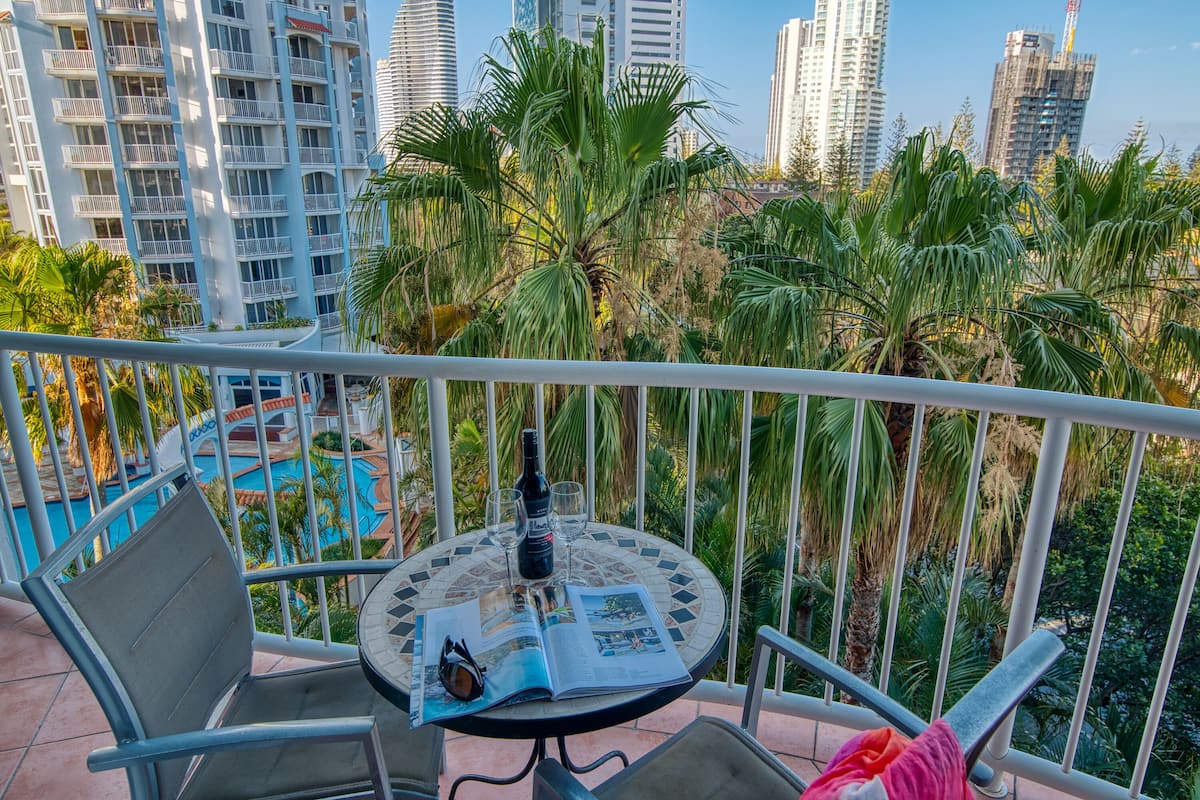 A balcony with a table, chairs, a bottle, glasses, and a magazine.