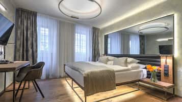 A modern hotel room with a bed, bedside table, chair, desk, and a large mirror.