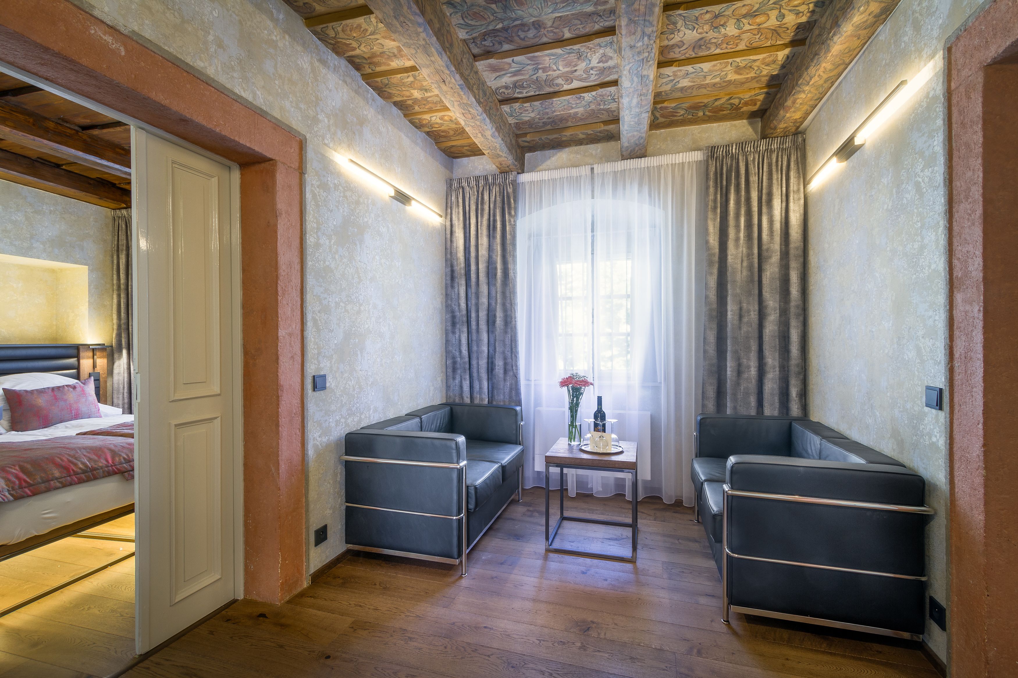Ein Zimmer mit einem Bett, zwei Sofas, einem kleinen Tisch mit einer Vase und einem Fenster mit Vorhängen.