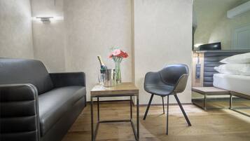 A modern room with a black leather sofa, a small wooden table with a vase of flowers, and a grey chair.