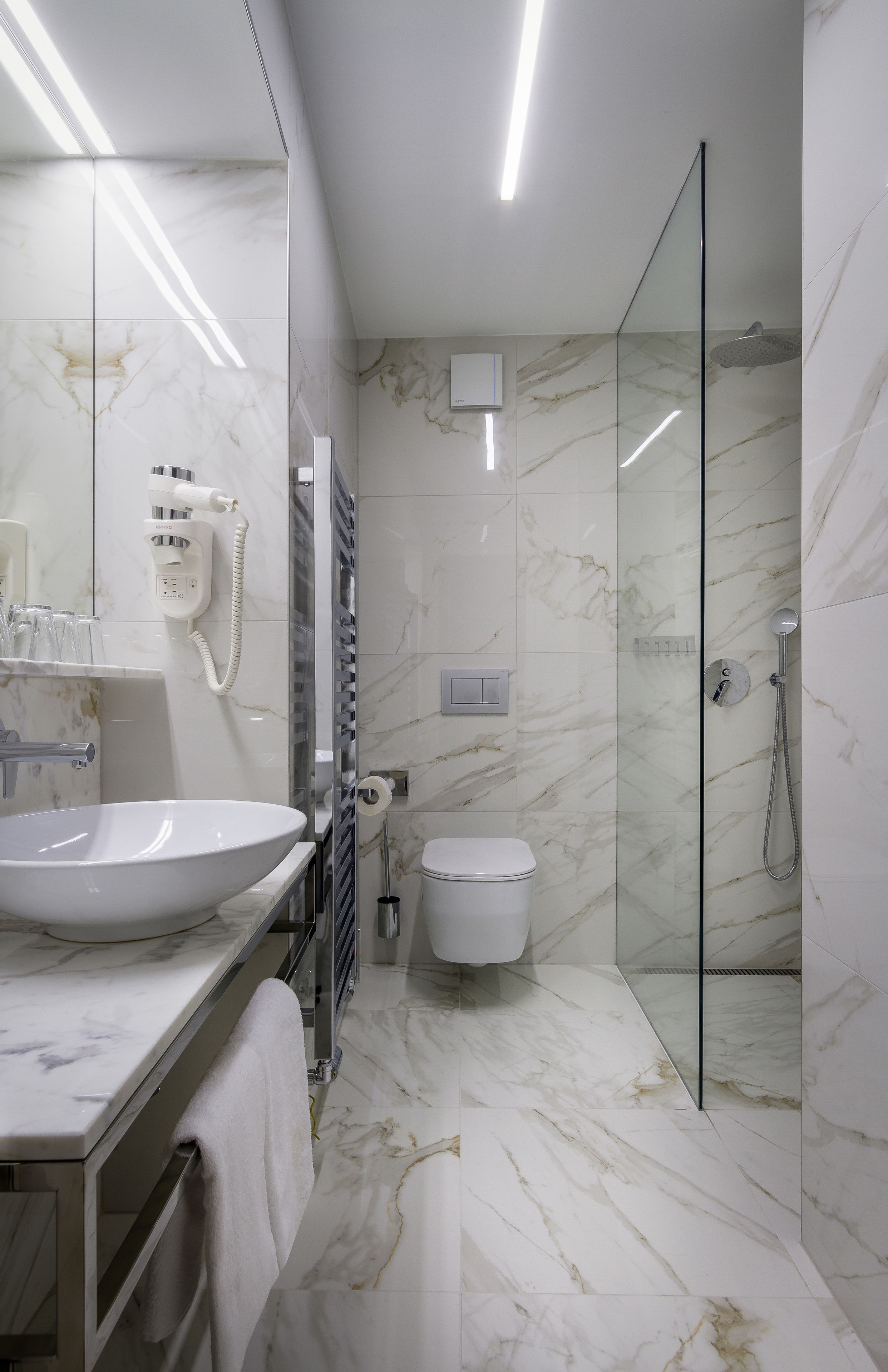 A modern bathroom with a large marble sink, a glass shower enclosure, and a toilet.