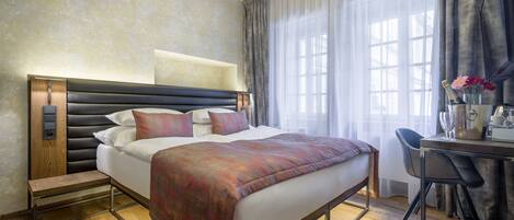 A hotel room with a large bed, a desk with a chair, and a window with curtains.