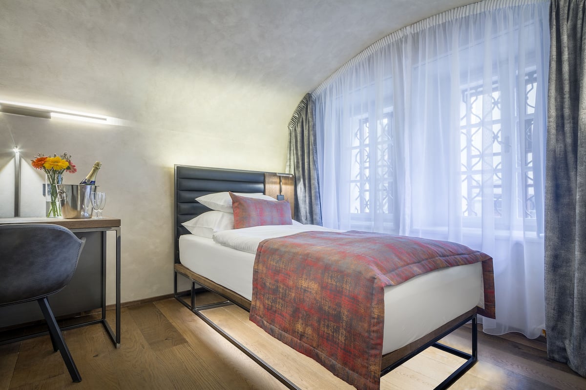 A modern hotel room with a bed, a desk, and a chair.