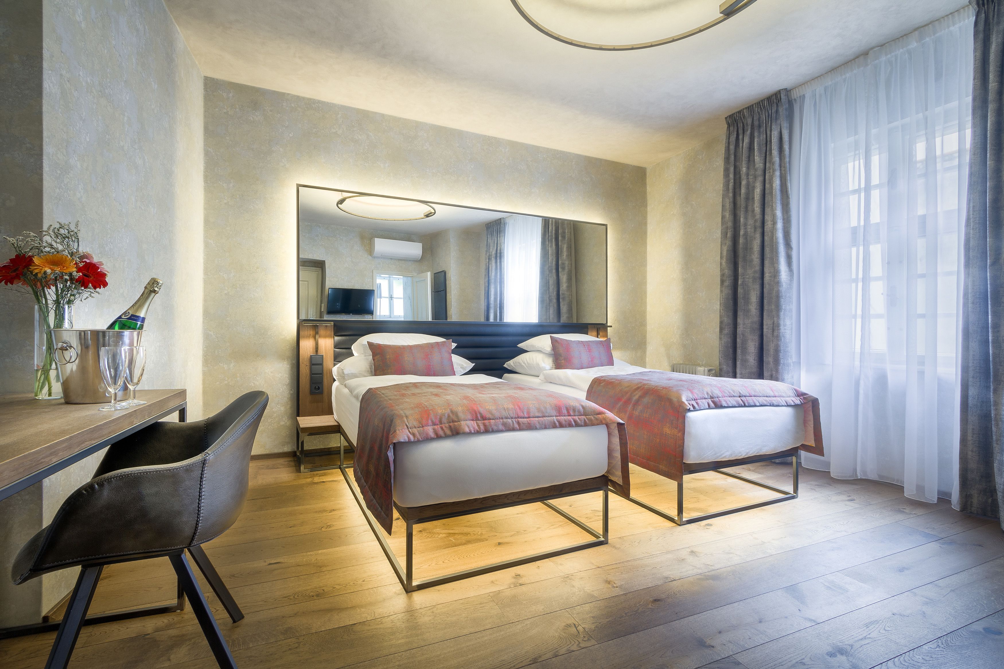 A modern hotel room with two beds, a desk, and a chair.