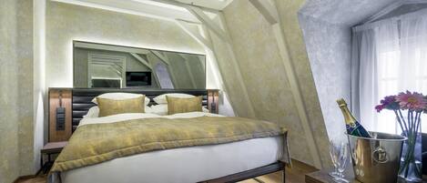 A modern bedroom with a large bed, a bedside table with a champagne bottle and glass, and a mirror above the bed.