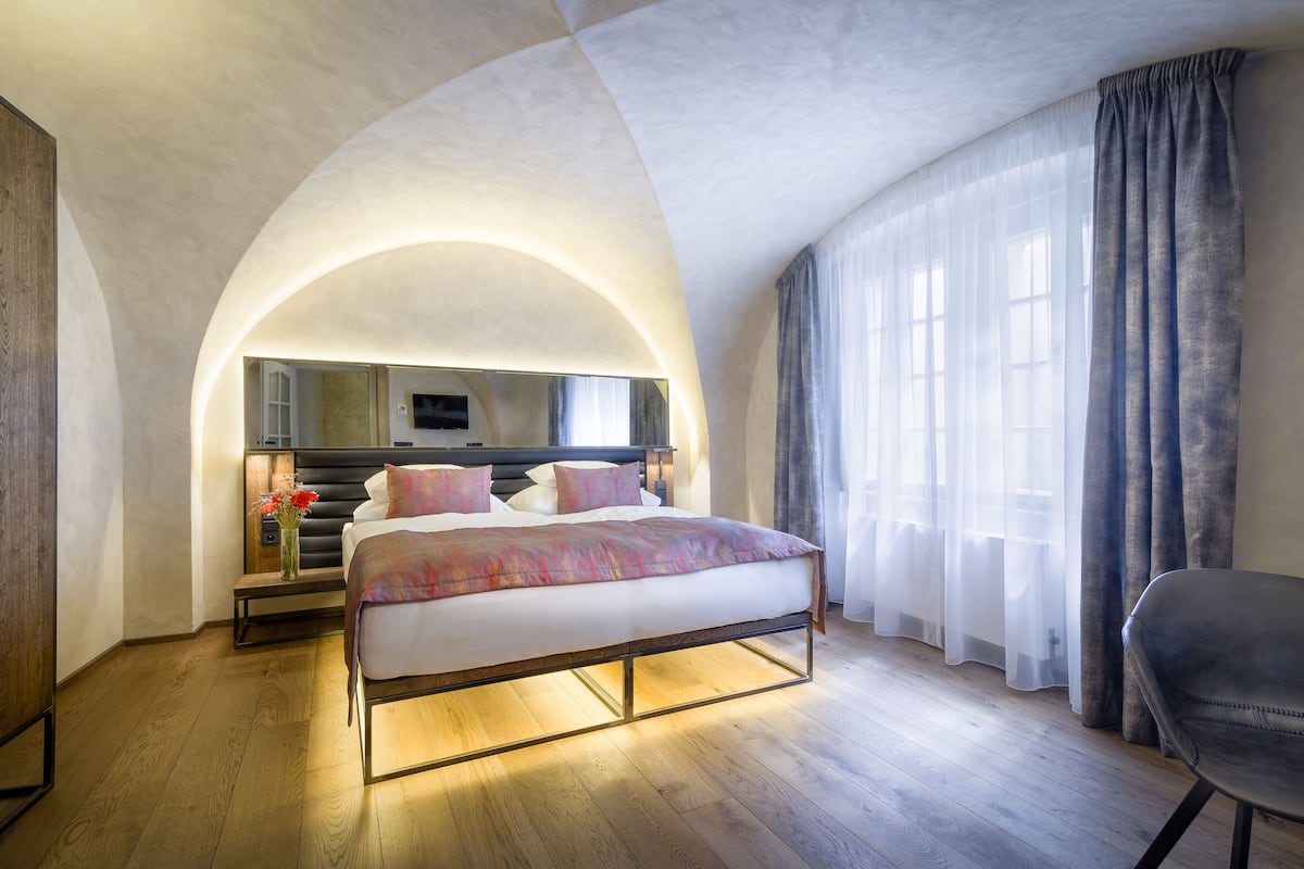 A modern bedroom with a large bed, a bedside table, a mirror, and a chair.