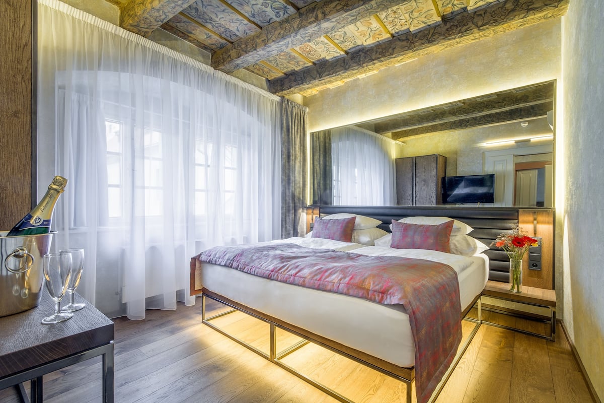 A hotel room with a bed, a TV, a nightstand with a vase, and a bottle of champagne.