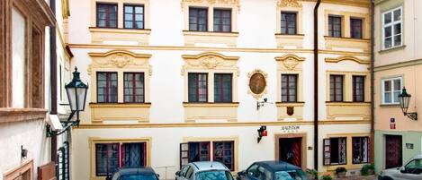 Un patio con pavimento de adoquines, tres coches estacionados y un edificio con fachada ornamentada en amarillo y rojo.