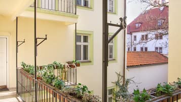 A covered balcony with a metal railing, potted plants, and a view of adjacent buildings.