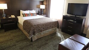 A hotel room with a large bed, two bedside tables with lamps, a flat-screen TV, a dresser, and a small seating area. - Staybridge Suites Silicon Valley by IHG (Milpitas)