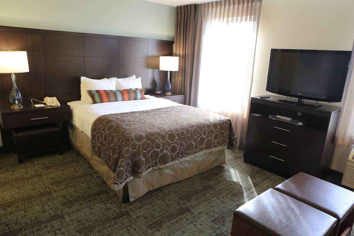 A hotel room with a large bed, two bedside tables with lamps, a flat-screen TV, a dresser, and a small seating area.