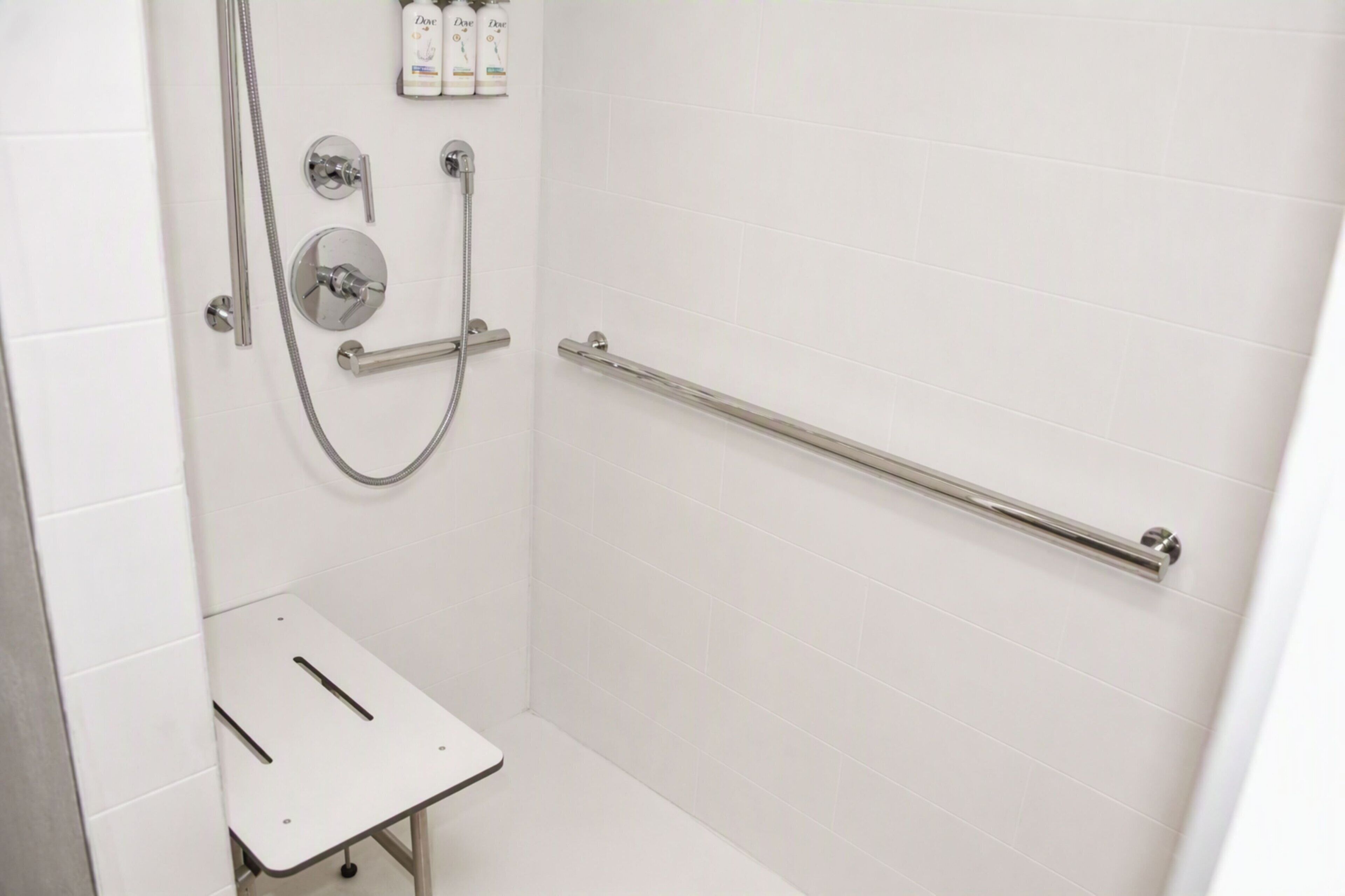 A shower with a handheld showerhead, a handheld shower attachment, and a handheld shower hose. There is a grab bar installed on the wall for support.