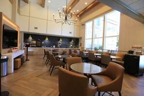 Ein modernes Café-Interieur mit runden Tischen, Stühlen, einer Kaffeemaschine und einem großen Fenster, das für natürliches Licht sorgt.