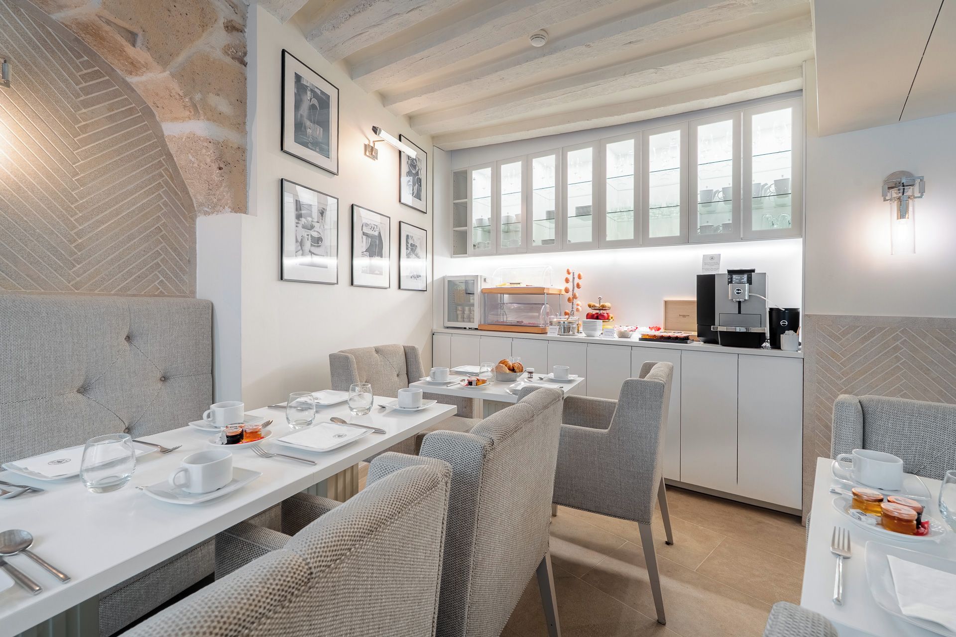 Un comedor moderno con mesas blancas, sillas tapizadas en gris y una barra de desayuno con una cafetera.