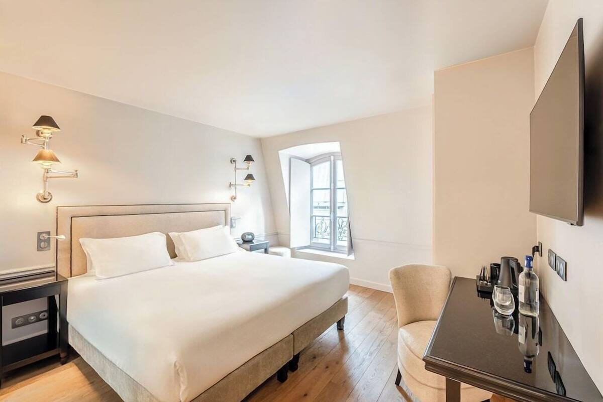 A hotel room with a bed, bedside table, lamp, chair, and a TV.