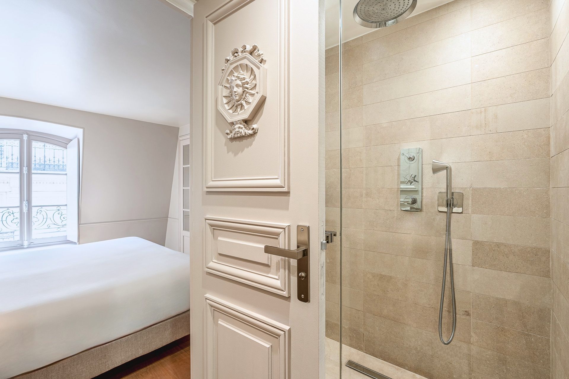 A hotel room with a bed, a door with a decorative emblem, and a shower with a handheld showerhead.