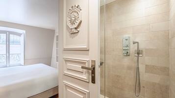 A hotel room with a bed, a door with a decorative emblem, and a shower with a handheld showerhead.